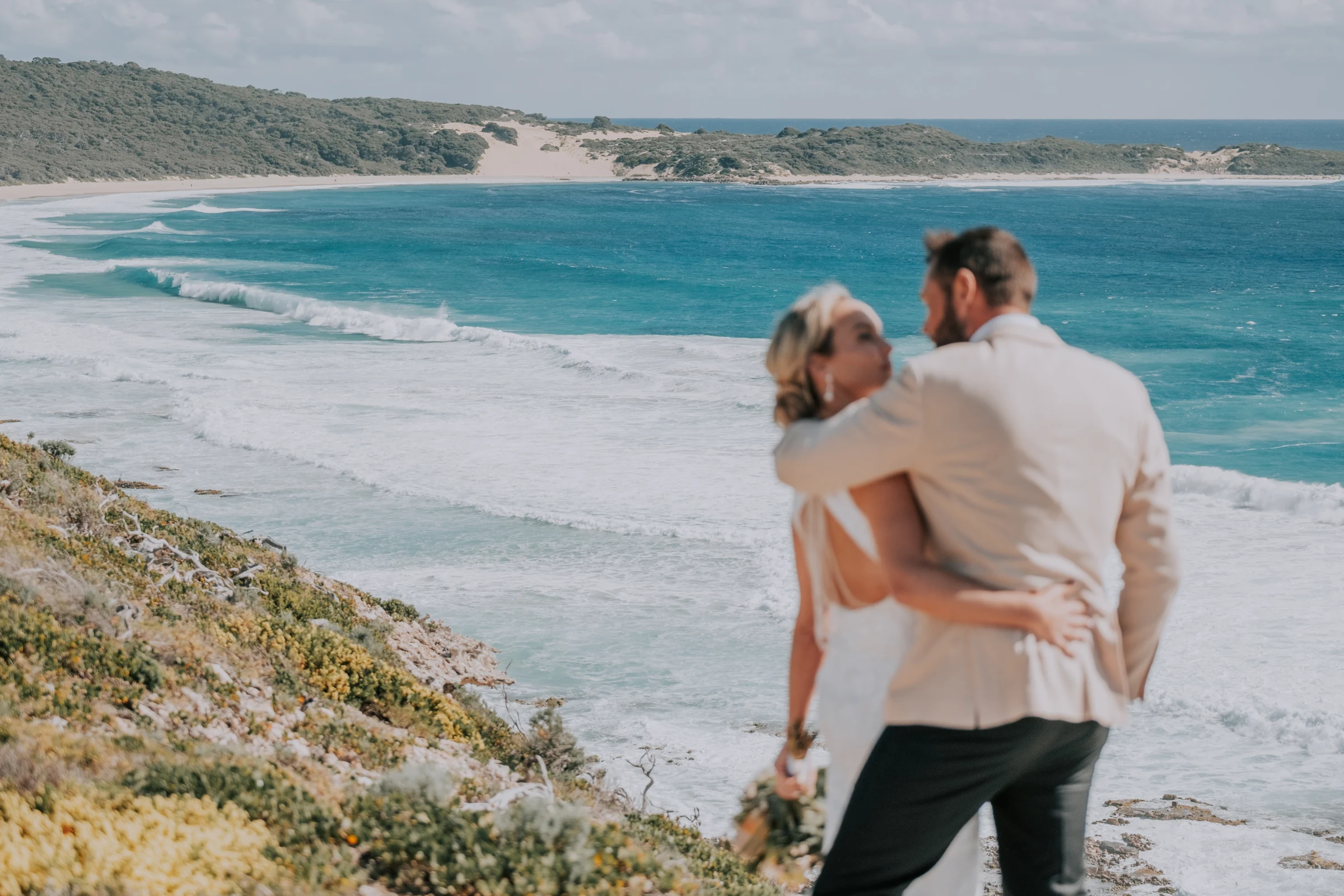 Victoria and Luck embracing on the clifftop, the curve of Injidup Beach stretching out behind them