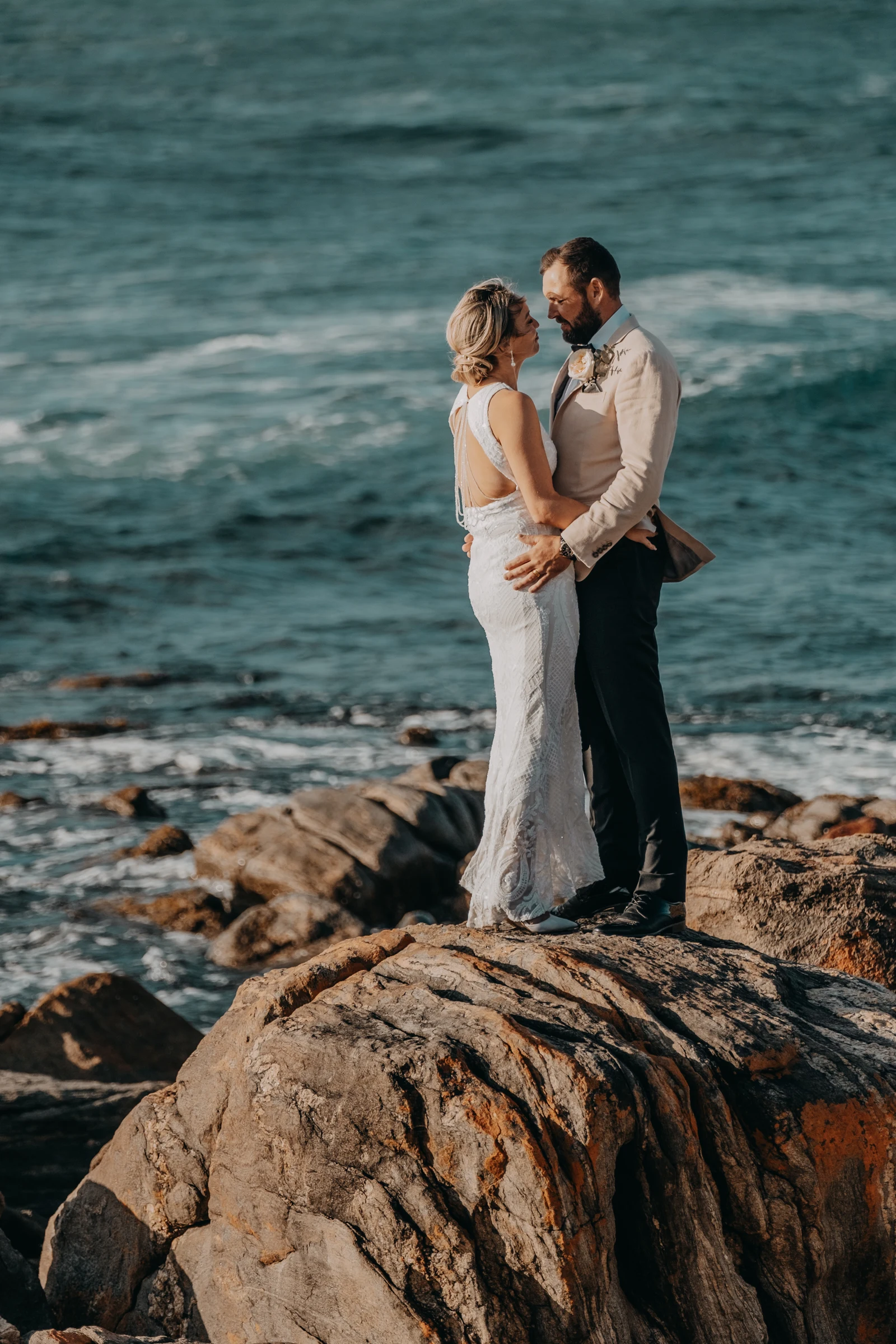 Victoria and Luck embracing on top of a large boulder, ocean stretching behind them