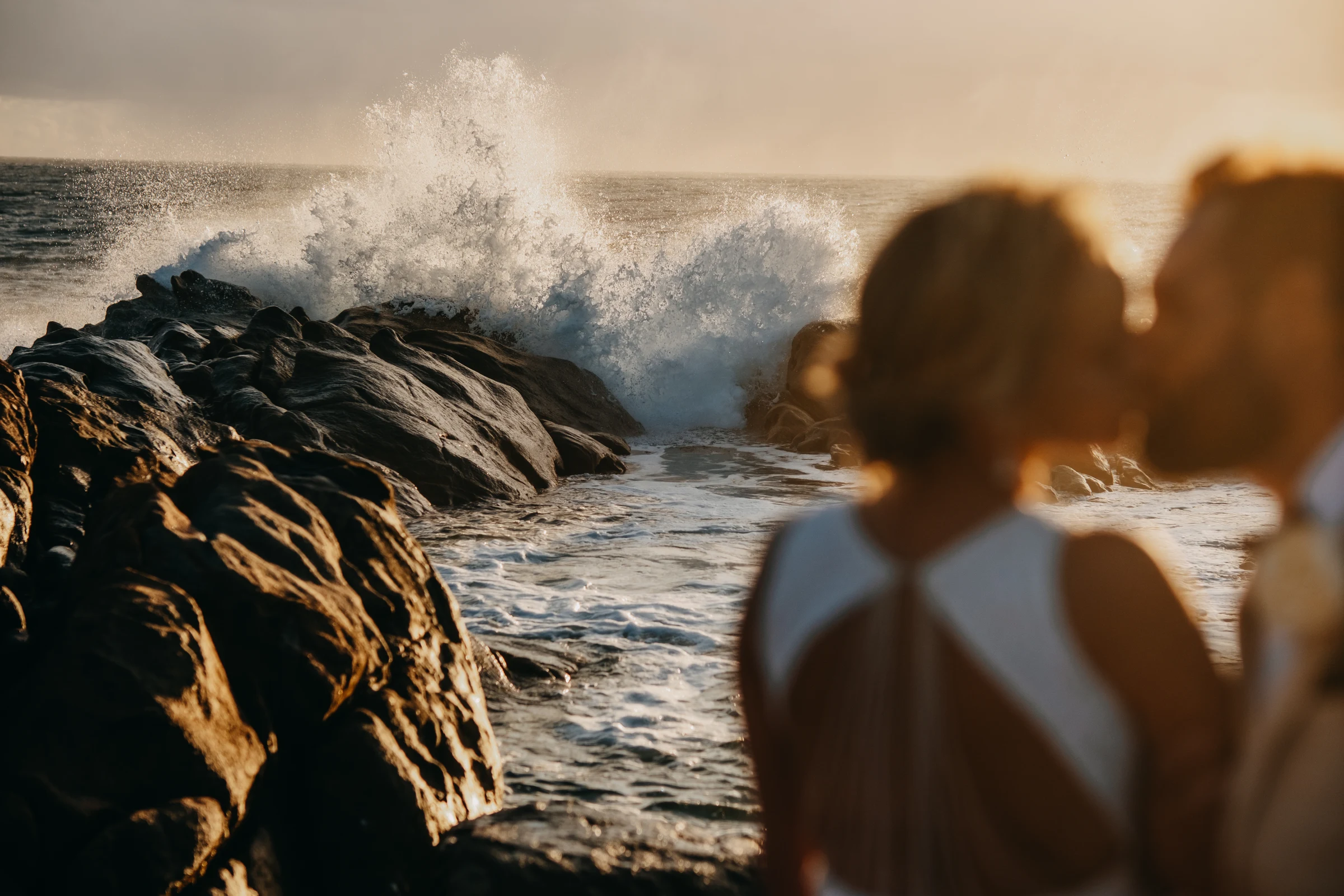 A wave crashing against the rocks at Injidup Beach with Victoria and Luck silhouetted together in the golden evening light
