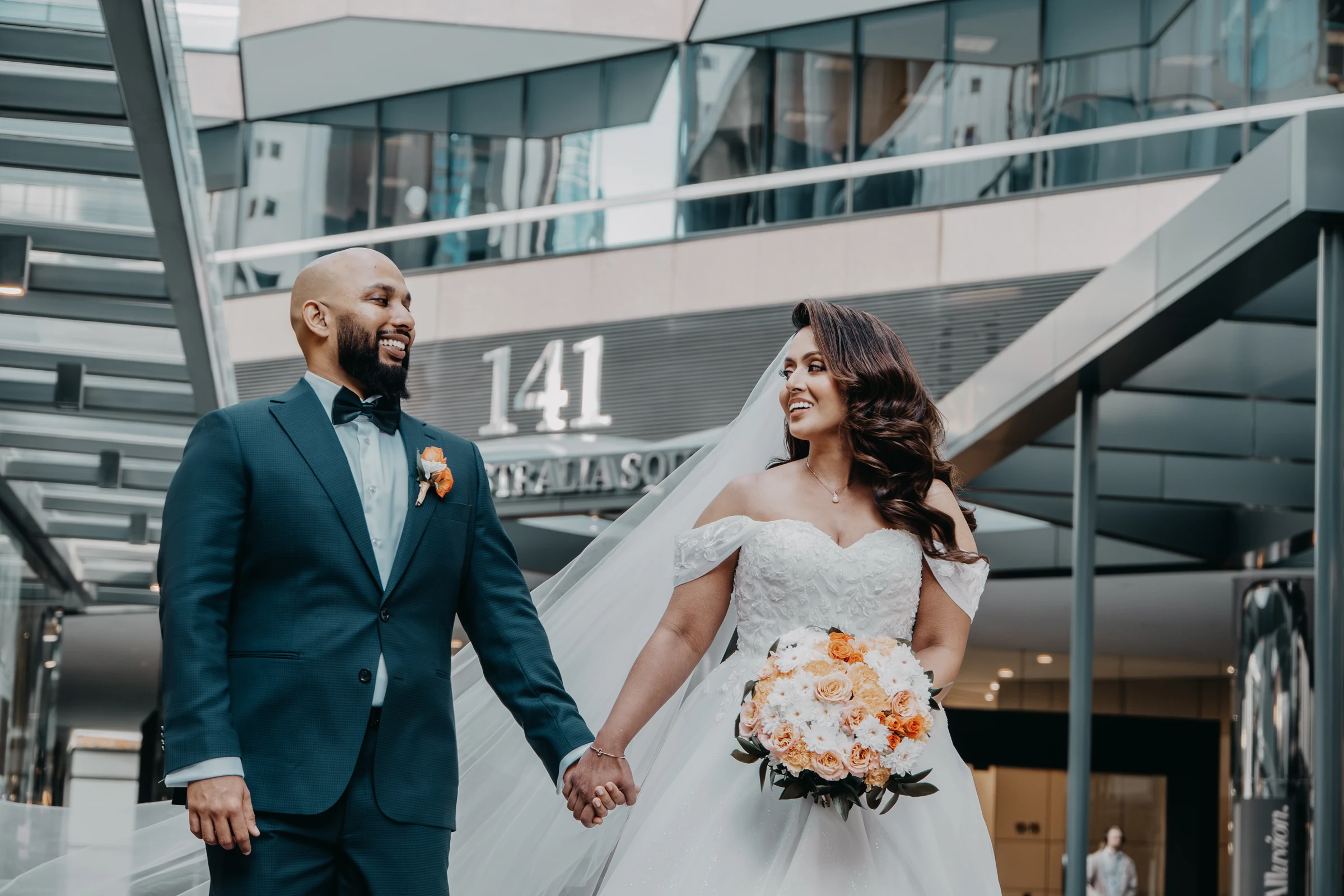 Betsy and Jibin walking hand in hand past the '141' building in the Perth CBD