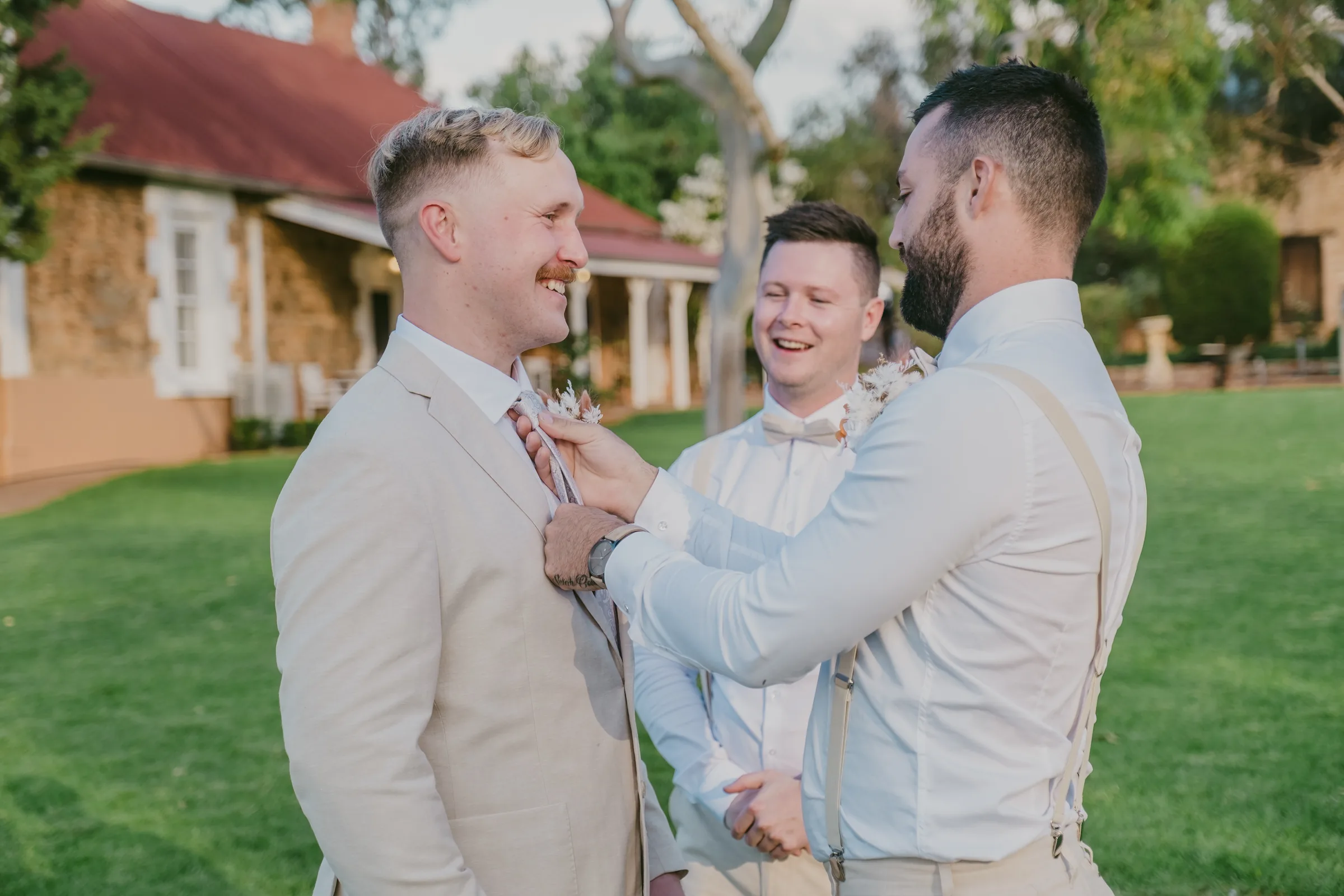 Lachie laughing with his groomsmen while having his tie straightened before the ceremony at Buckland Estate
