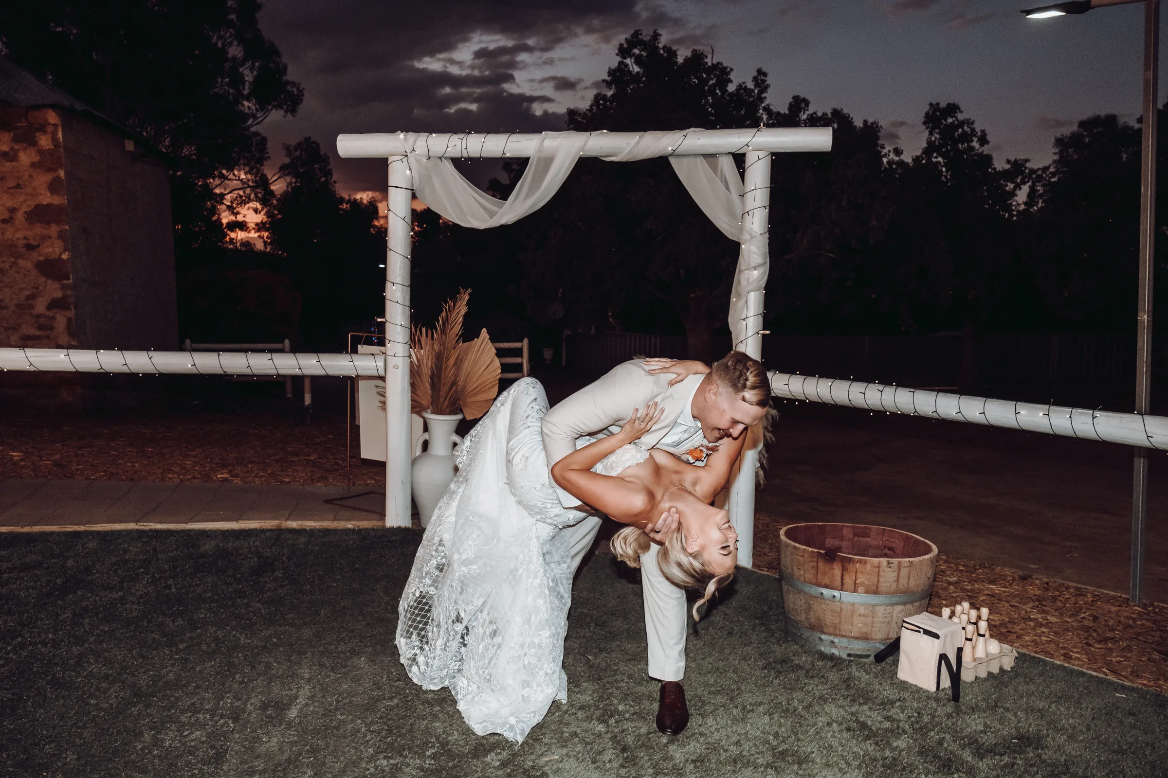 Lachie dipping Grace for a kiss under a lit floral arbour at their Buckland Estate reception