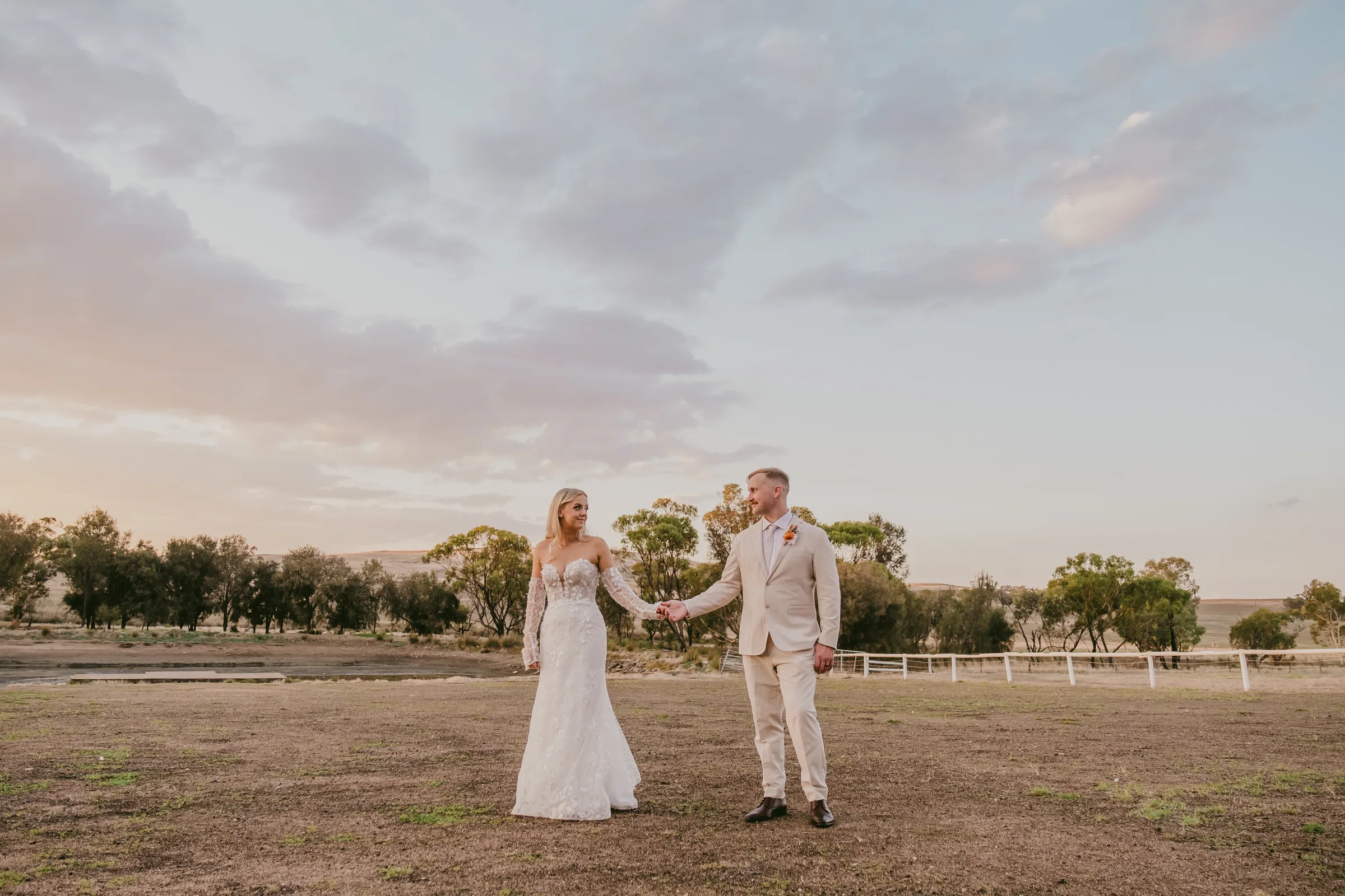 Grace and Lachie walking hand in hand across the paddocks at Buckland Estate at golden hour
