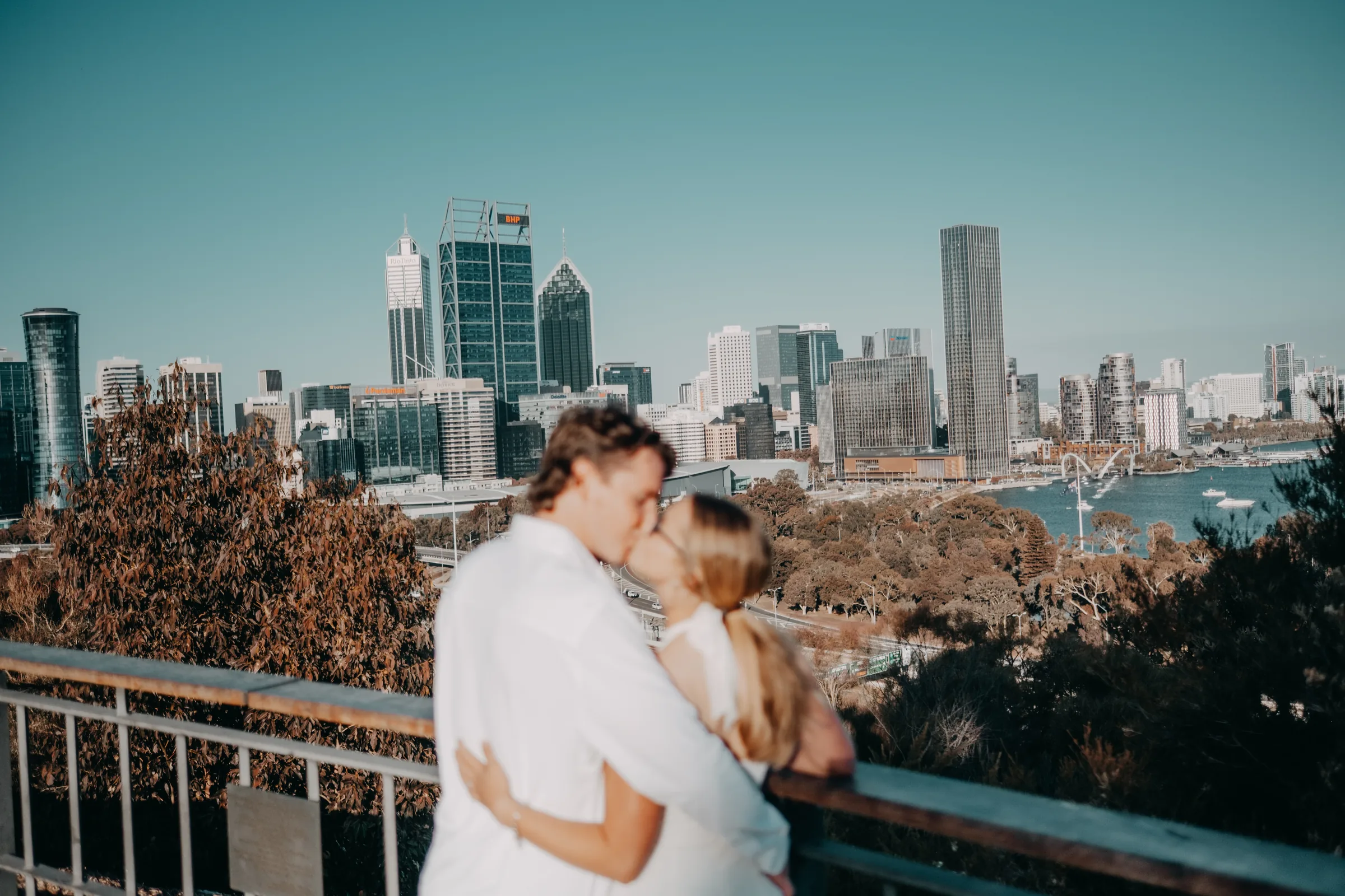 Kayla and Brett embracing on the Kings Park lookout with the Perth city skyline behind them at golden hour