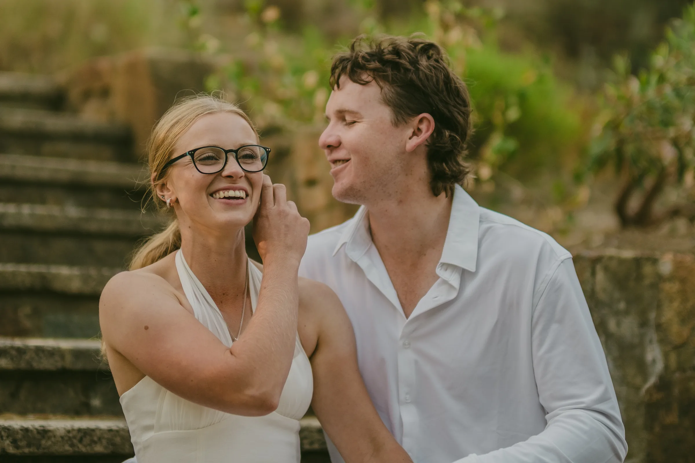 Kayla and Brett laughing together on a stone stairway at Kings Park during golden hour