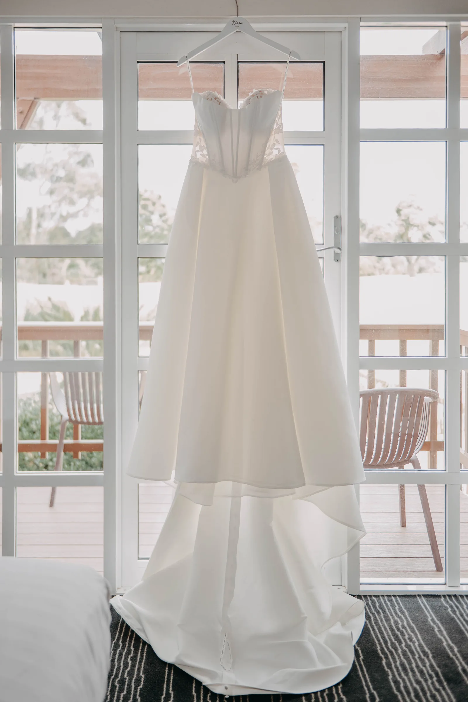 Kirra's wedding dress hanging in the window light before her wedding at The Vines Resort