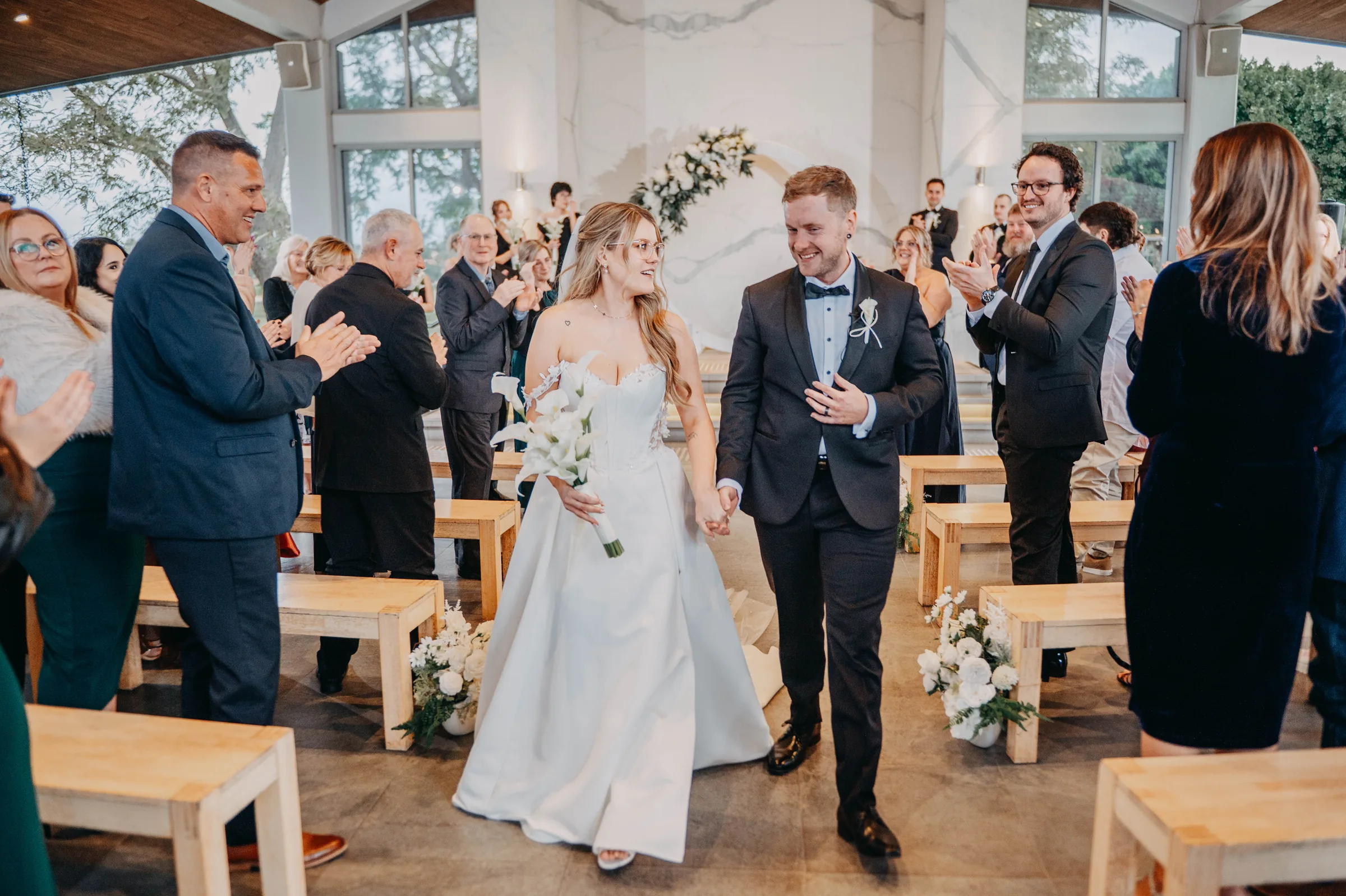 Kirra and Mitch walking back up the aisle together as newlyweds at the Garden Pavilion