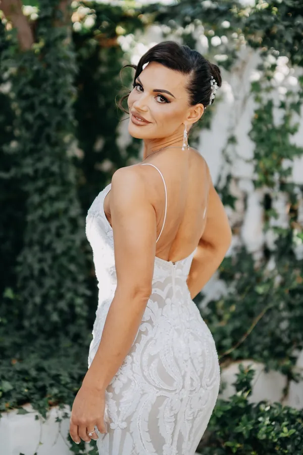Katia glancing back over her shoulder in her lace wedding dress against an ivy-covered wall