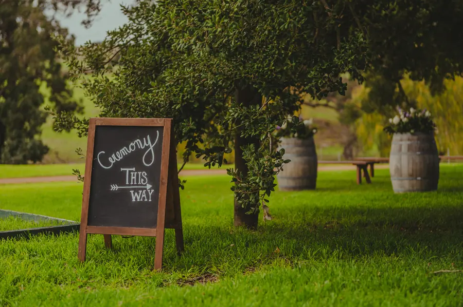 A chalkboard 'Ceremony This Way' sign among the trees at Dalmore Farm