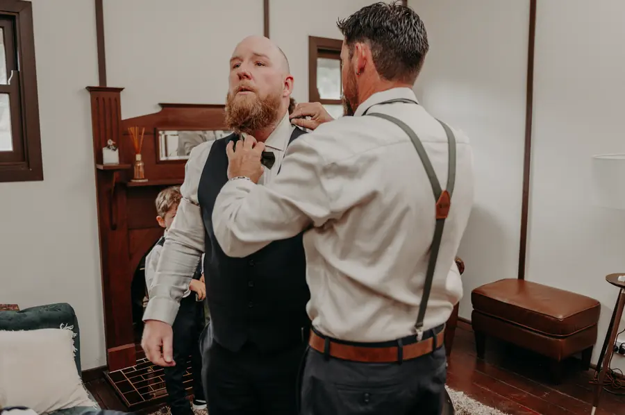 A groomsman helping Ben adjust his bow tie while getting ready at Dalmore Farm