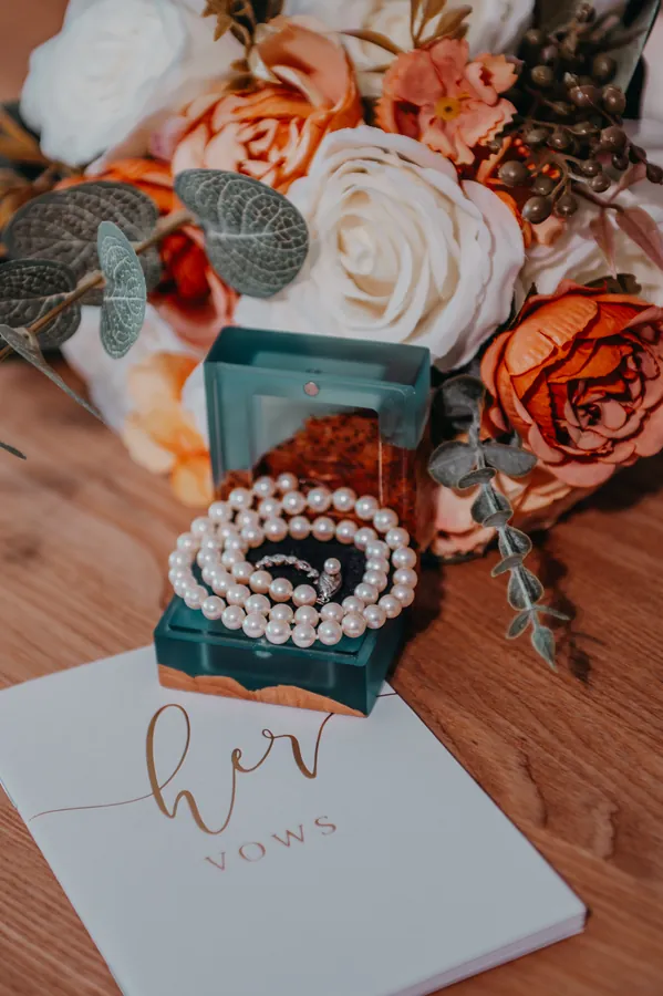 Bridal flat lay of pearl jewellery and a 'Her Vows' book resting on the bouquet before the ceremony