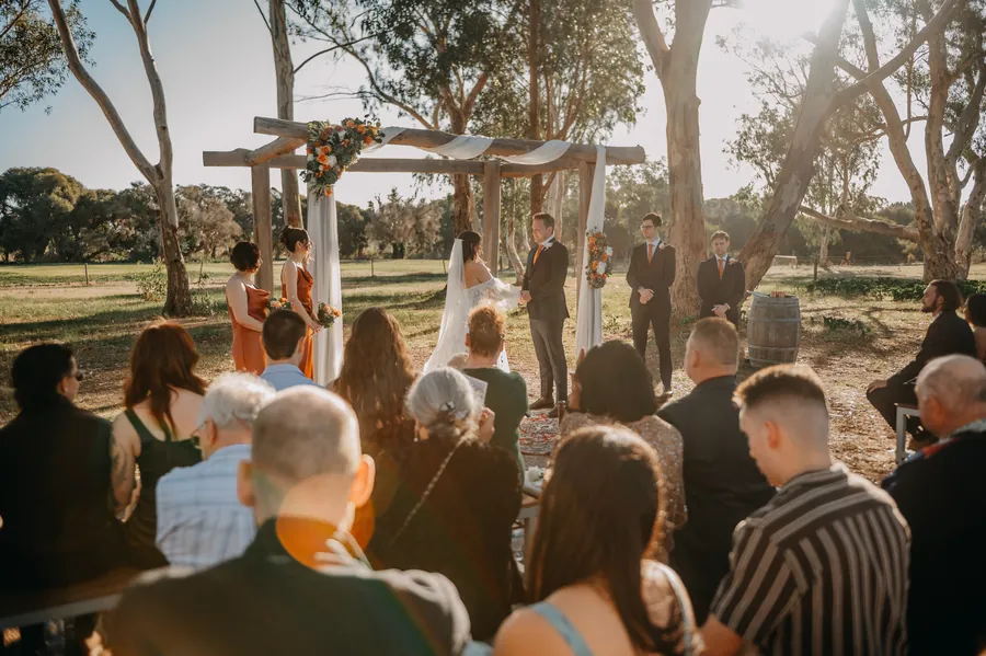 Wide shot of the wedding ceremony under a rustic timber arbour among the gum trees at The Barn, Hopeland