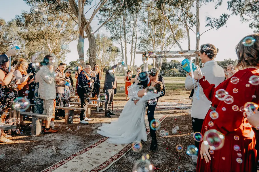 Bride and groom kissing surrounded by floating bubbles under gum trees at The Barn Hopeland wedding ceremony
