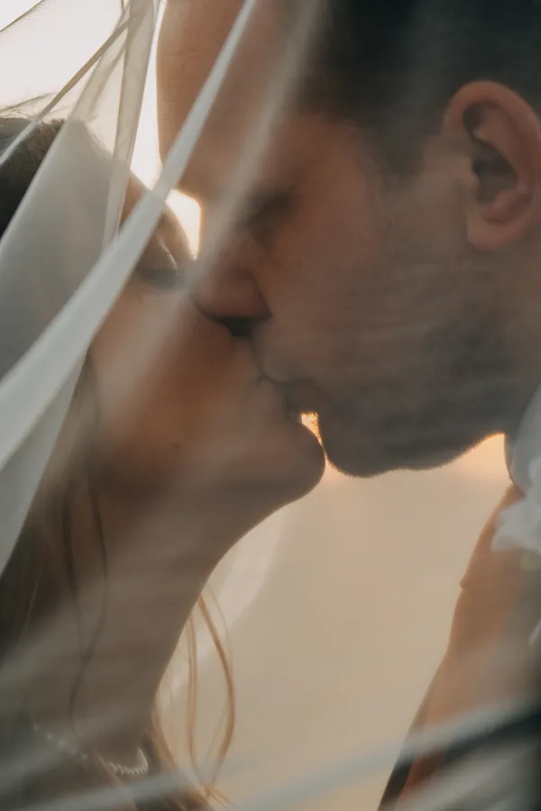 Extreme close-up of the bride and groom kissing under the veil with sun flare