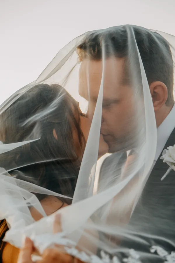 Bride and groom kissing under the veil, close-up portrait lit by the setting sun
