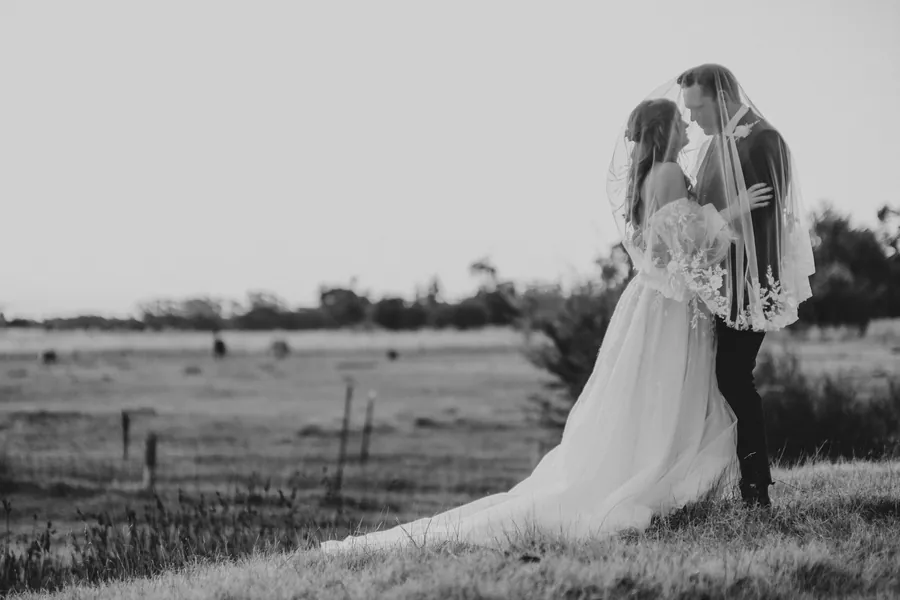 Black and white wide shot of the bride and groom kissing under the veil in an open paddock at Hopeland