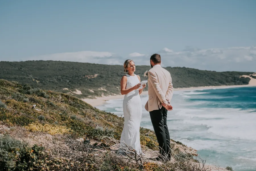 Victoria and Luck standing together with their backs to camera, looking out over Injidup Beach during their vows
