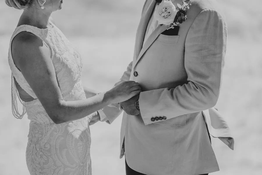 Black and white close-up of Victoria and Luck's joined hands against Luck's jacket during the ceremony