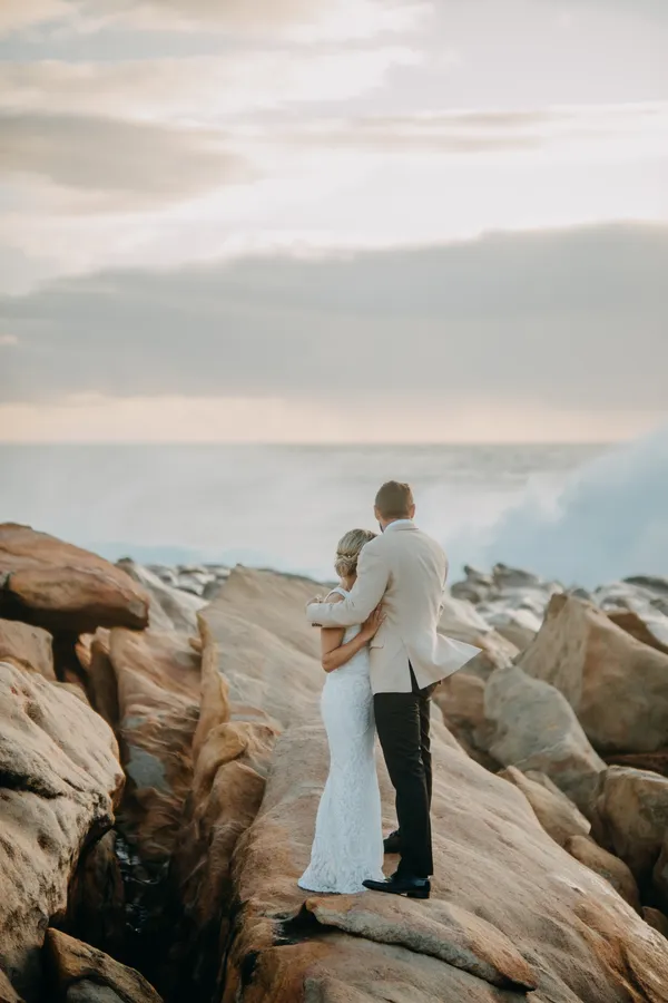 Victoria and Luck standing together on the rocky ledge, looking out at the ocean as the light fades