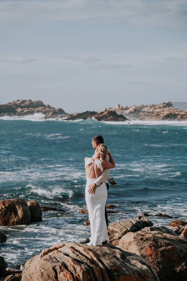 Victoria and Luck embracing on the rocks, looking out over the ocean at Injidup Beach