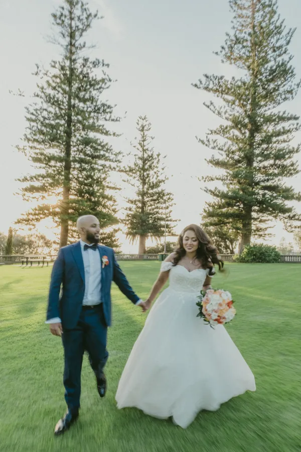 Betsy and Jibin walking hand in hand across the lawn at Cottesloe Civic Centre as the sun begins to set