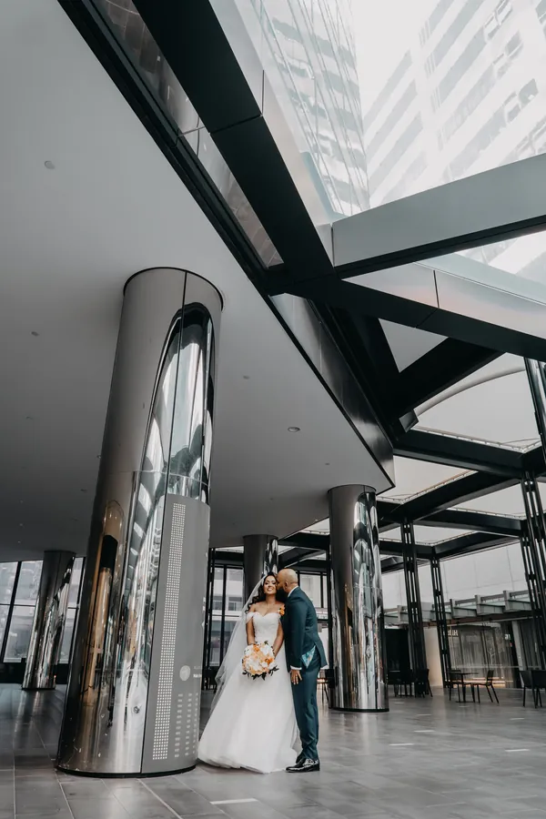 Betsy and Jibin walking hand in hand beneath the mirrored columns of a Perth CBD building