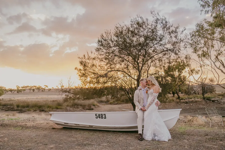 Grace and Lachie posing beside a rustic wooden rowboat prop at sunset on the Buckland Estate paddocks
