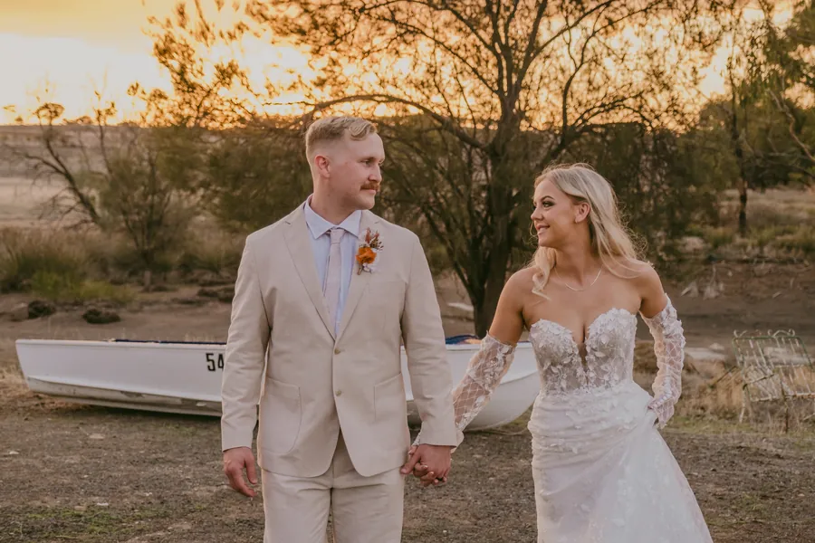 Grace and Lachie holding hands beside the rowboat prop as the sun sets over Buckland Estate