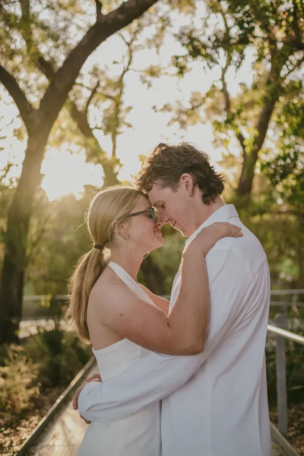 Kayla and Brett embracing under backlit trees at Kings Park, golden hour light behind them