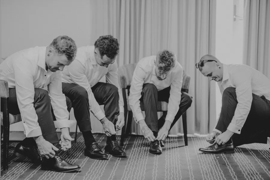 Black and white photo of Mitch and his groomsmen tying their shoes before the wedding