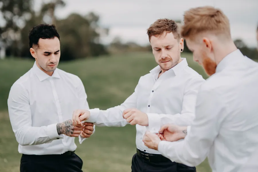 Groomsmen helping each other with their shirt cuffs on The Vines Resort lawn